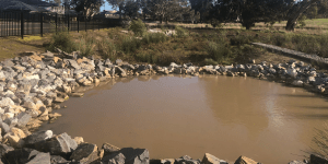 Big pond of brown-coloured water surrounded by rocks
